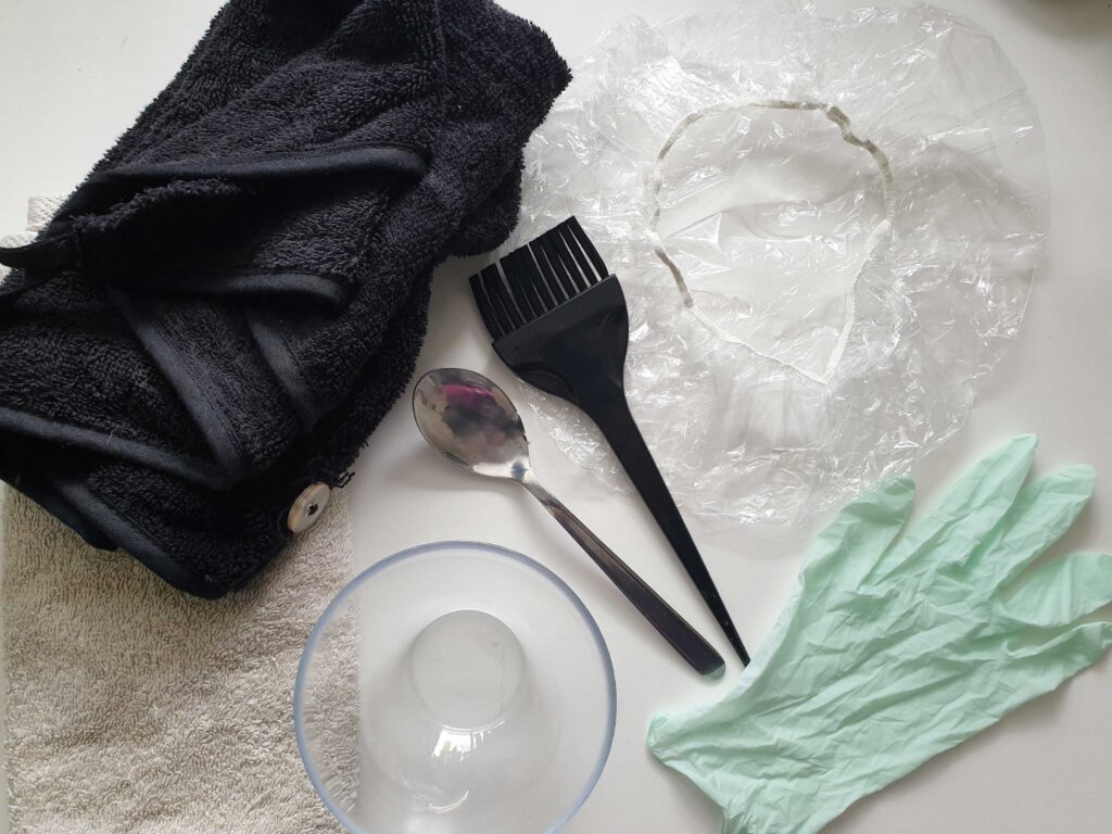 Flat lay photograph of equipment used for henna hair dye - bowl, spoon, hair tint brush, shower cap, gloves, towel, hair towel wrap. Photo by One Woman's Notebook.
