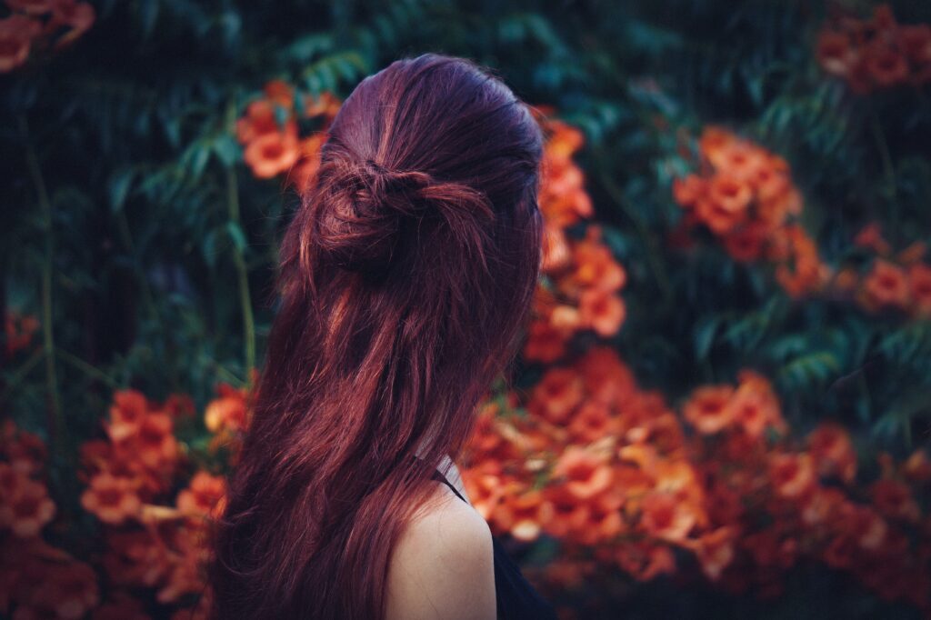 Woman with deep red hair, head turned away, facing a view of orange flowers. Photo by Štefan Štefančík on Unsplash
