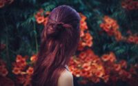 Woman with deep red henna hair, head turned away, facing a view of orange flowers. Photo by Štefan Štefančík on Unsplash
